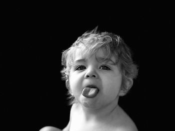 Portrait of cute boy sticking out tongue against black background