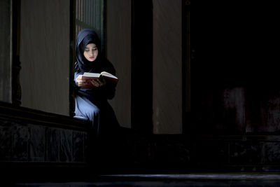 Woman reading book while sitting on window sill