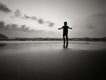 Rear view of silhouette boy standing at beach against sky