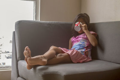 Girl drinking coffee while sitting on sofa at home
