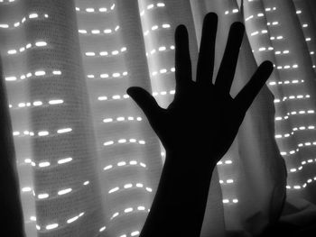 Silhouette hand against illuminated curtain at night