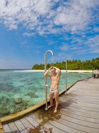 Full length of shirtless man bathing under shower on pier by sea