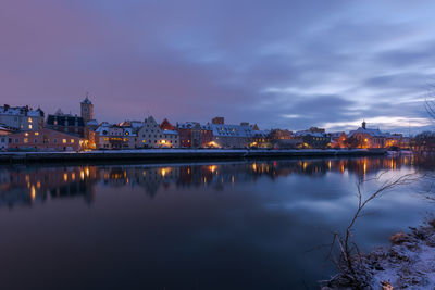 Reflection of illuminated buildings in lake against sky at dusk