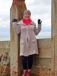 Smiling woman in warm clothes standing on pier at sea