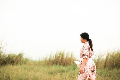 Side view of woman walking on grass against sky