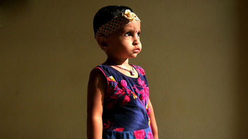 Cute girl looking away while standing against wall