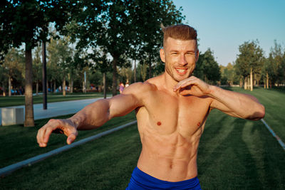 Portrait of shirtless man standing against trees