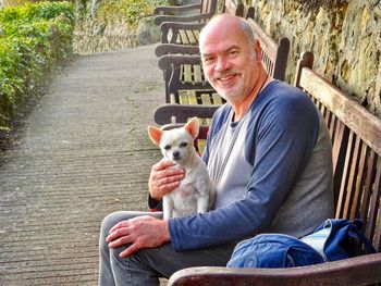 Portrait of smiling man with dog sitting on bench