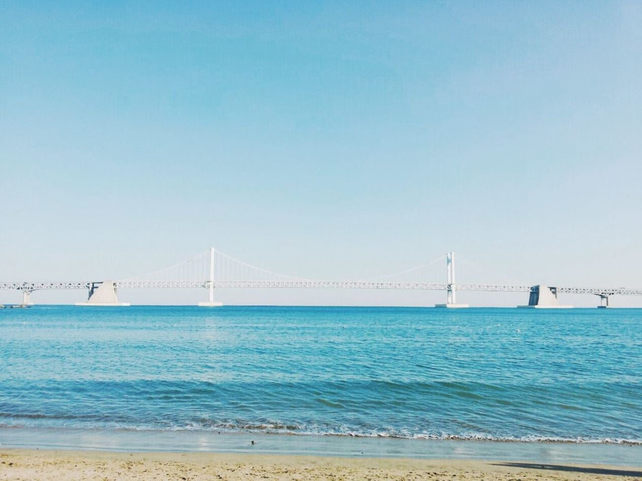 connection, sea, suspension bridge, water, bridge - man made structure, clear sky, engineering, built structure, copy space, architecture, bridge, golden gate bridge, travel destinations, transportation, tranquil scene, tranquility, beach, blue, tourism, scenics