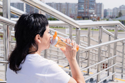 Portrait of woman drinking water from railing in city