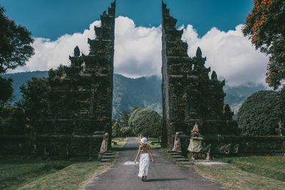 Rear view of woman walking amidst trees against sky