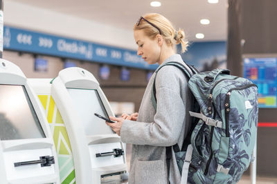 Smiling woman using smart phone while standing by atm machine