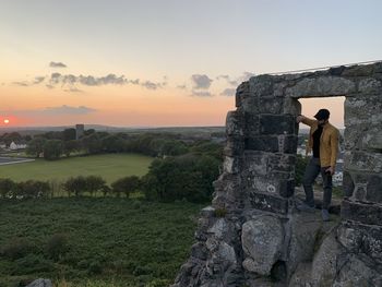 Rear view of man standing on field against sky during sunset