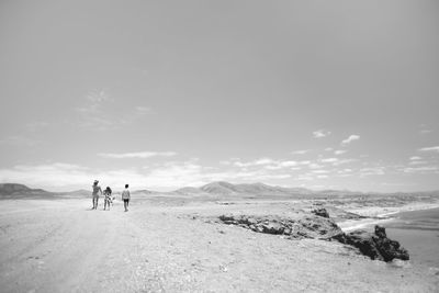 Rear view of family walking on beach against sky