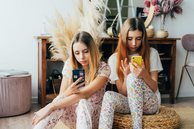 Young woman using phone while sitting on laptop