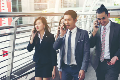 Colleagues using phones while walking on elevated walkway 