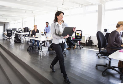 Mid adult businesswoman with laptop walking in office