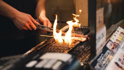 Midsection of person cooking meat on barbecue grill