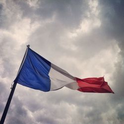 Low angle view of red flag against cloudy sky