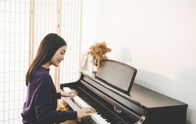 Side view of smiling woman playing piano at home