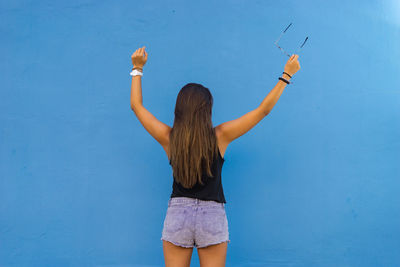 Rear view of teenage girl with arms raised standing against wall