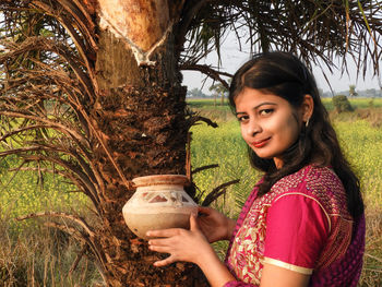 Portrait of smiling young woman holding container by tree 