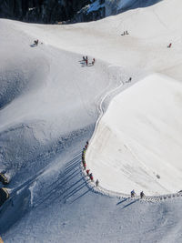 People skiing on snow covered landscape against cloudy sky