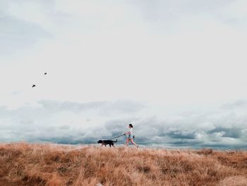 Woman with dog walking on field against sky