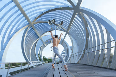 Rear view of shirtless man dancing on bridge