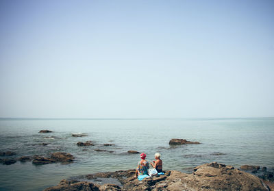 People on rocks by sea against clear sky