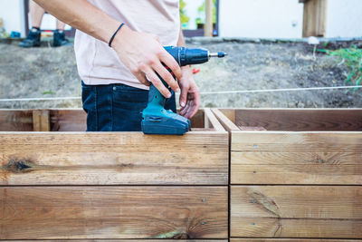 Midsection of man holding drill machine while standing by wooden structure