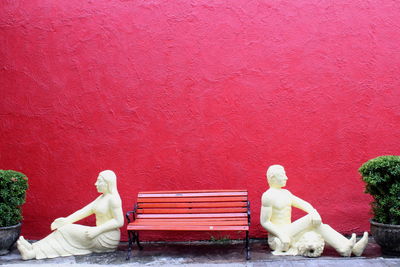 Statue of woman sitting on bench against red wall