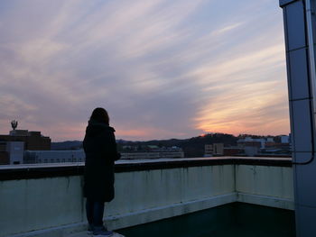 Woman standing by cityscape against sky during sunset