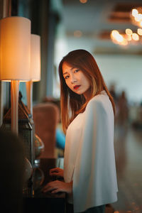 Side view portrait of young woman standing by illuminated lamps on table