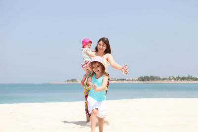 Happy woman with arms raised on beach against sky