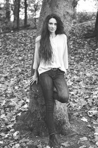 Portrait of young woman standing on tree trunk in forest