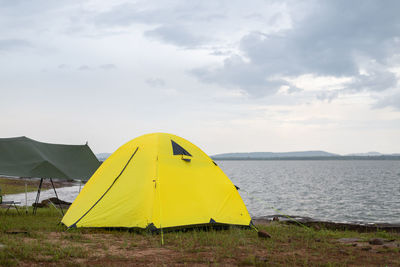 Yellow tent on land by sea against sky