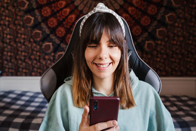 Young woman using mobile phone against wall