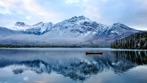 A lonesome canoe floats on a freezing water lake with surrounding snow covered mountains. 