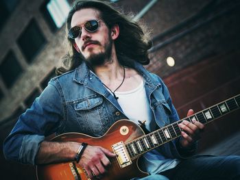 Bearded man playing guitar while sitting outdoors