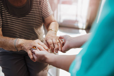 Midsection of healthcare worker holding hands of senior woman at nursing home
