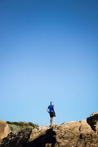 Teenager standing on rock against clear blue sky