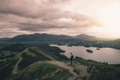 Woman standing on mountain against cloudy sky during sunset