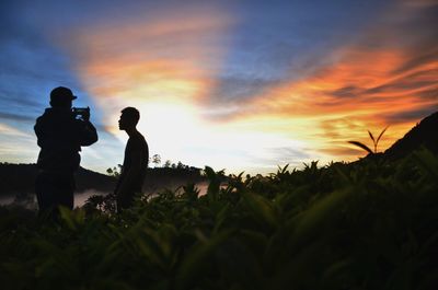 Silhouette friends standing on field against cloudy sky during sunset