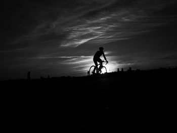 Low angle view of silhouette man riding bicycle on field against sky during sunset