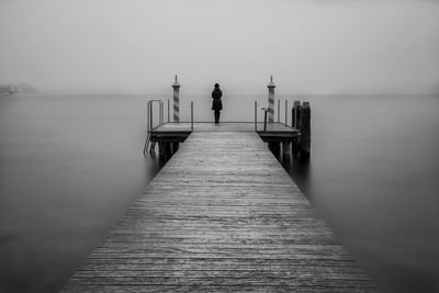 Rear view of woman standing on pier over sea against sky