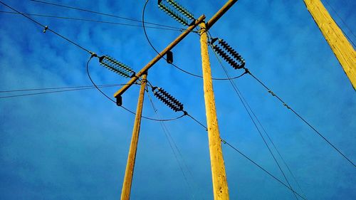 Low angle view of electricity pylon against blue sky