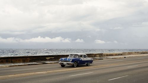 Car on road by sea against sky