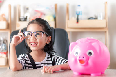 Girl sitting by piggy bank at home
