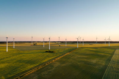 Drone view of windmills on grassy field against clear sky